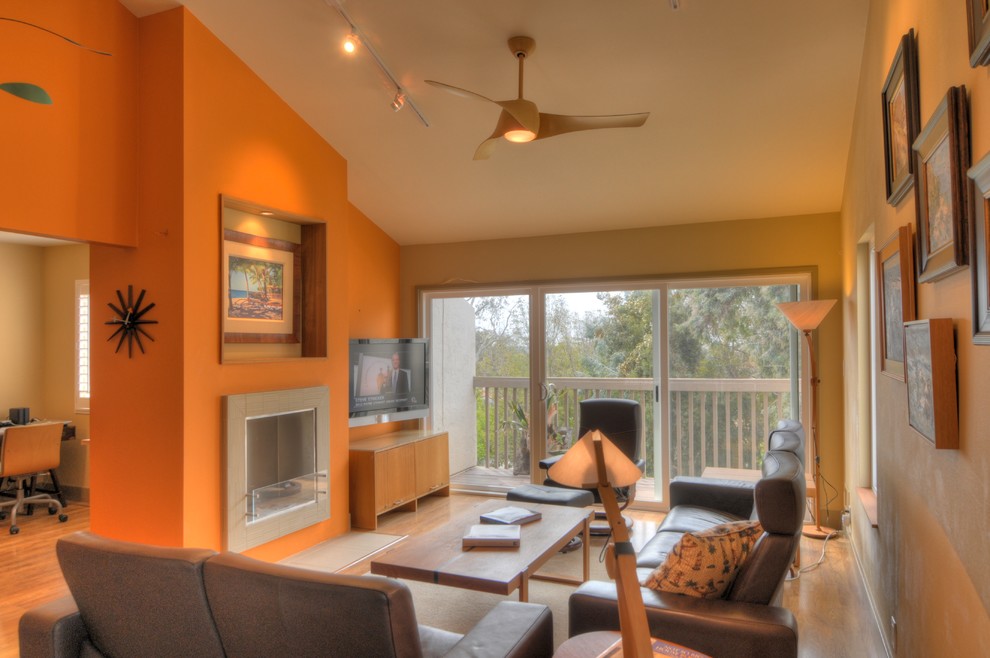 Cette image montre un salon minimaliste avec un mur orange, sol en stratifié et un manteau de cheminée en carrelage.