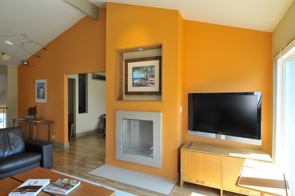 Foto de salón moderno con parades naranjas, suelo laminado y marco de chimenea de baldosas y/o azulejos