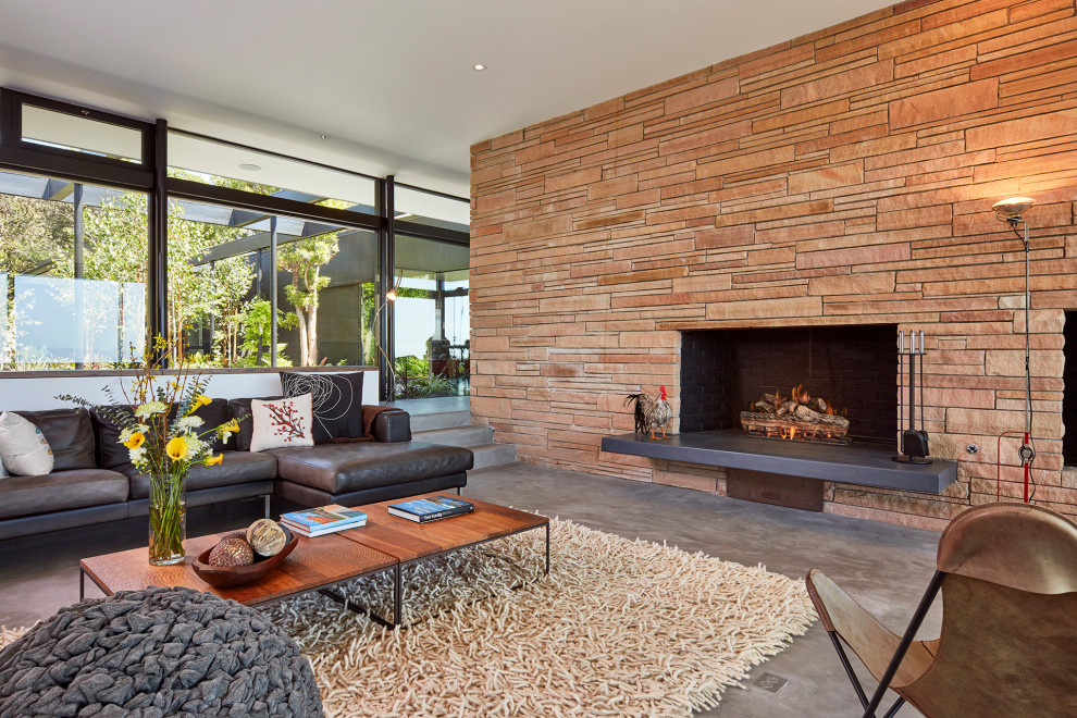 サンフランシスコにあるミッドセンチュリースタイルのおしゃれなLDK (コンクリートの床、標準型暖炉、石材の暖炉まわり、グレーの床、黒いソファ) の写真
