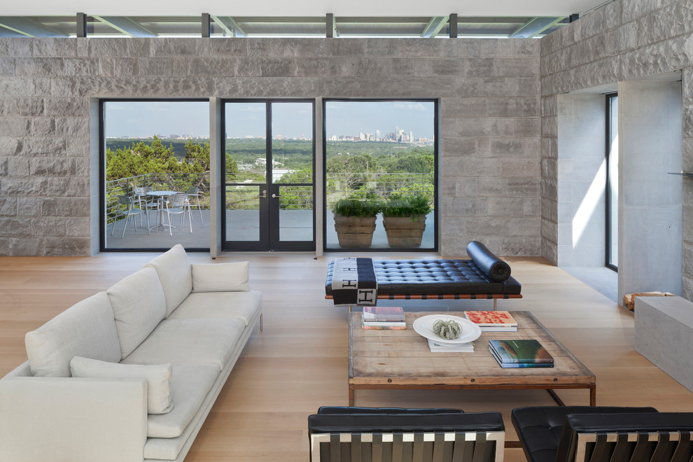Modelo de salón para visitas abierto moderno grande con suelo de madera clara, televisor independiente, paredes grises y piedra