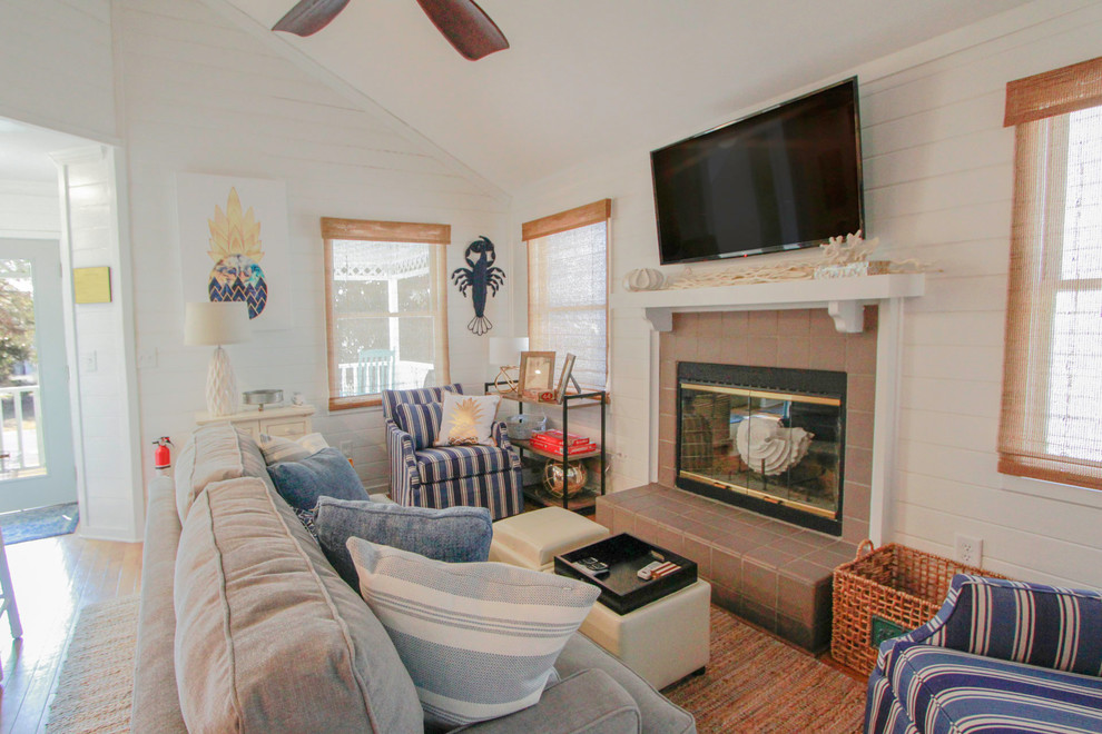 На фото: открытая гостиная комната среднего размера в морском стиле с белыми стенами, паркетным полом среднего тона, стандартным камином, фасадом камина из плитки, телевизором на стене и разноцветным полом с