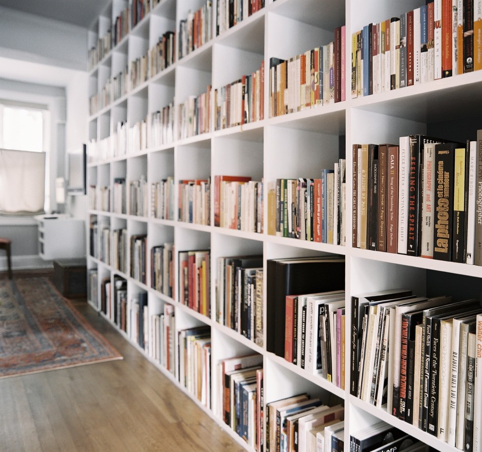 Imagen de biblioteca en casa abierta actual grande sin chimenea y televisor con paredes blancas y suelo de madera en tonos medios
