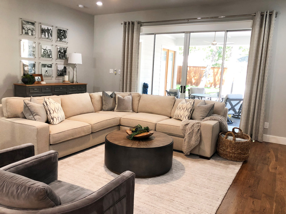 This is an example of a large traditional open plan living room in Dallas with grey walls, medium hardwood flooring, a standard fireplace, a tiled fireplace surround, a wall mounted tv and brown floors.