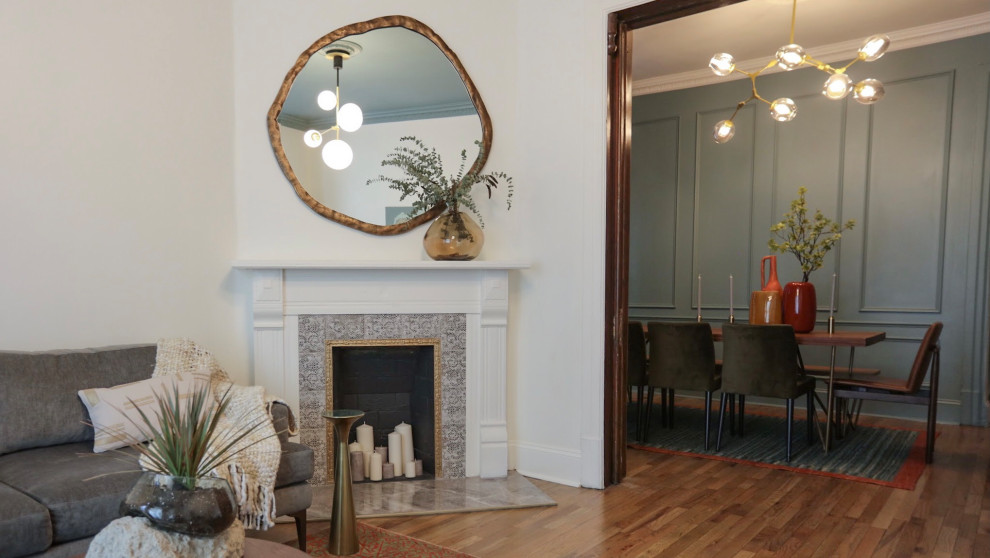 На фото: гостиная комната в стиле неоклассика (современная классика) с белыми стенами, деревянным полом, угловым камином, фасадом камина из плитки и коричневым полом