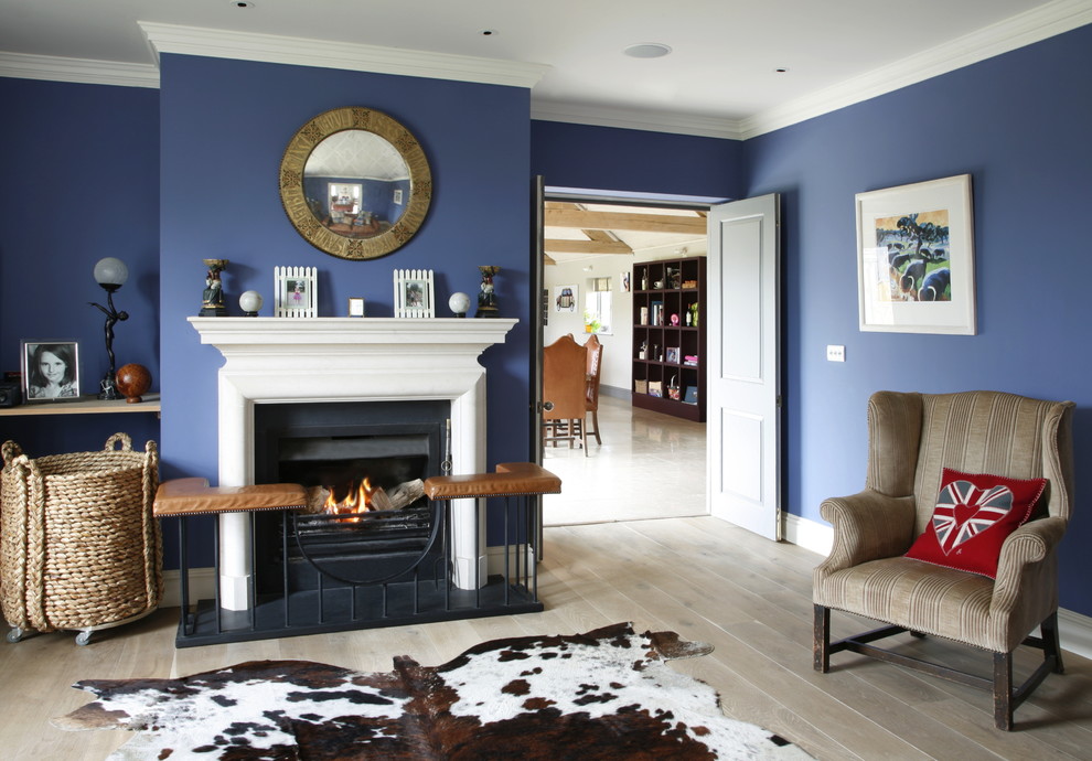 This is an example of a country formal enclosed living room in London with blue walls, light hardwood flooring and a standard fireplace.