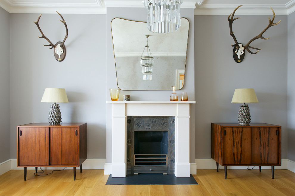 Photo of a medium sized midcentury formal enclosed living room in London with grey walls, medium hardwood flooring, a standard fireplace, a stone fireplace surround and brown floors.