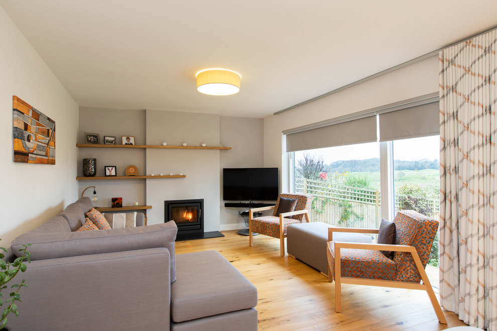 Aménagement d'un petit salon contemporain ouvert avec un mur gris, parquet clair, un poêle à bois, un manteau de cheminée en plâtre et un téléviseur indépendant.