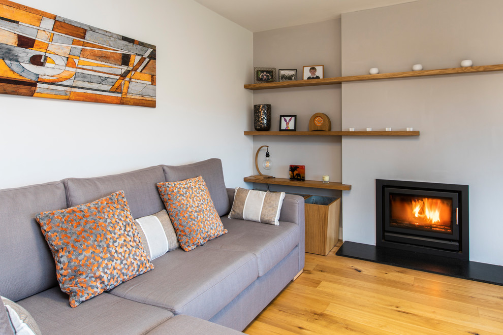 Idee per un piccolo soggiorno design aperto con pareti grigie, parquet chiaro, stufa a legna, cornice del camino in intonaco e TV autoportante