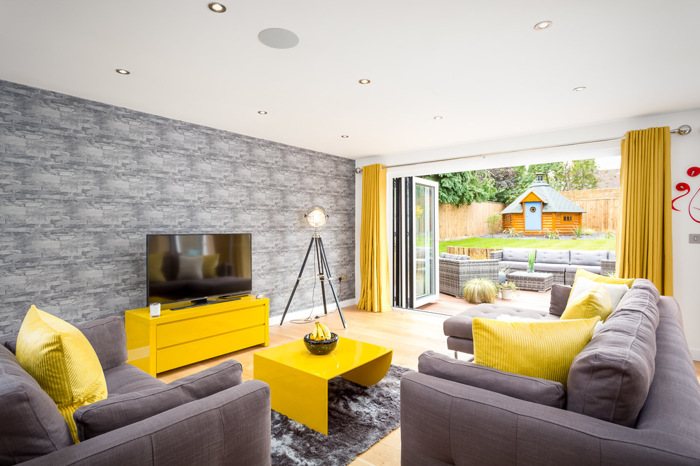 Large contemporary grey and yellow enclosed living room in Gloucestershire with white walls, light hardwood flooring and a freestanding tv.