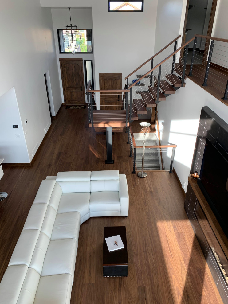 Exempel på ett stort modernt loftrum, med vita väggar, mellanmörkt trägolv, en standard öppen spis, en spiselkrans i trä, en väggmonterad TV och brunt golv