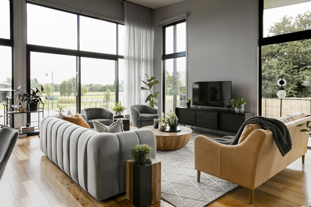 Modelo de salón abierto actual extra grande con paredes grises, suelo de madera en tonos medios, televisor independiente y suelo beige