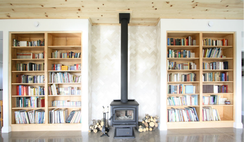 Diseño de biblioteca en casa abierta tradicional renovada de tamaño medio con paredes blancas, suelo de cemento, estufa de leña y marco de chimenea de baldosas y/o azulejos