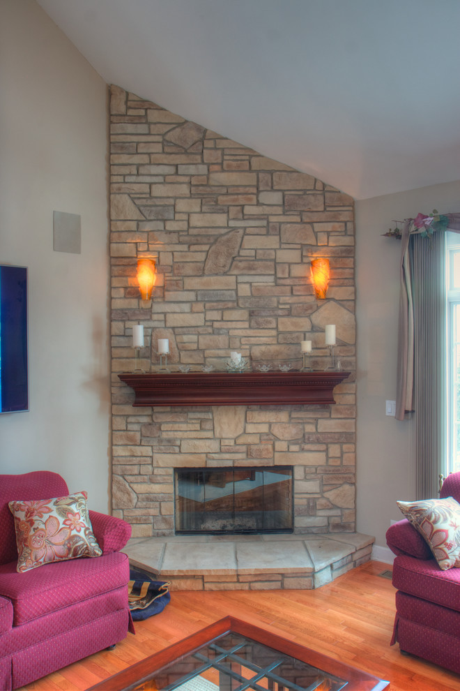 Imagen de salón abierto retro de tamaño medio sin televisor con paredes beige, suelo de madera clara, chimenea de esquina, marco de chimenea de piedra y suelo marrón