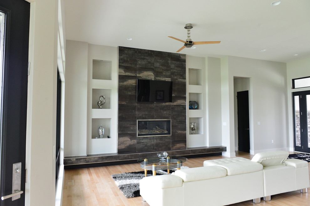 Пример оригинального дизайна: большая открытая гостиная комната в современном стиле с стандартным камином, телевизором на стене, белыми стенами, светлым паркетным полом и фасадом камина из металла