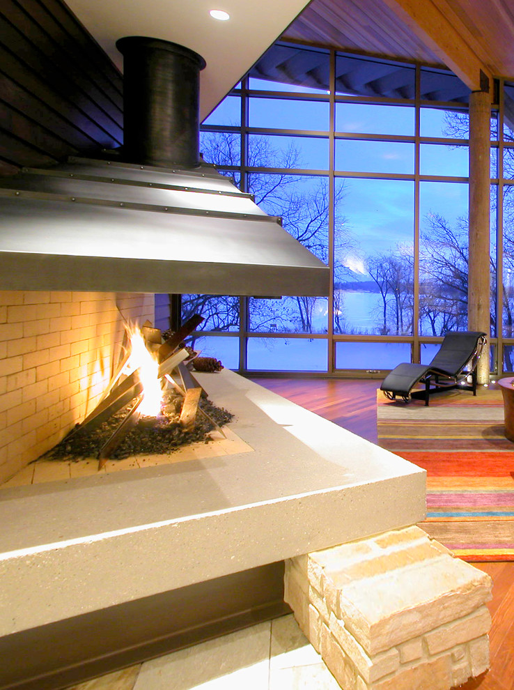 Cette photo montre un grand salon moderne ouvert avec une cheminée double-face, un manteau de cheminée en métal, un mur marron et parquet foncé.