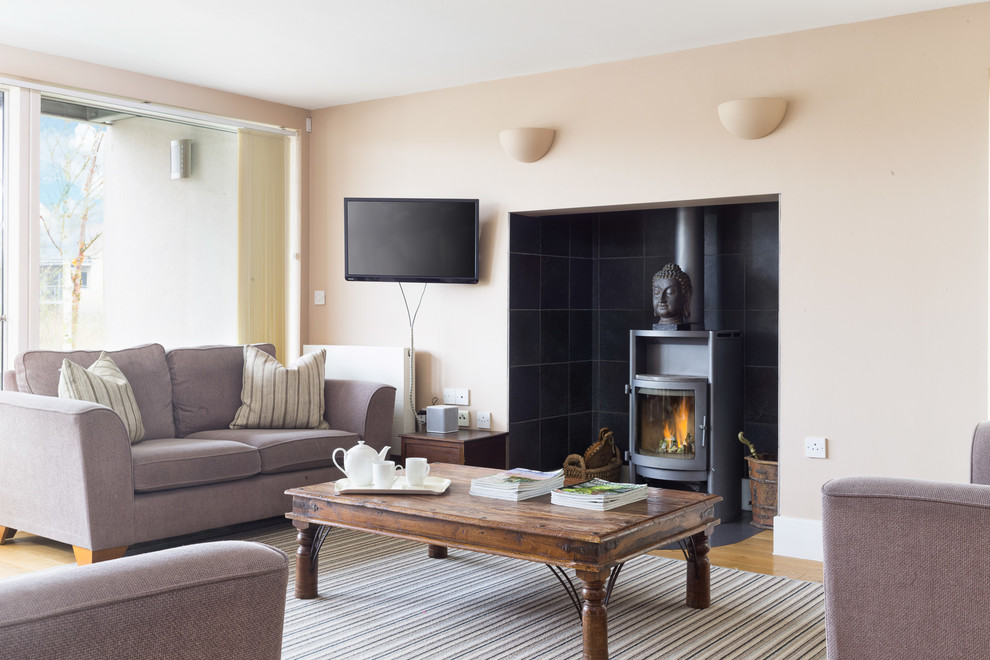 Medium sized contemporary enclosed living room in Gloucestershire with beige walls, light hardwood flooring, a wood burning stove, a tiled fireplace surround and beige floors.