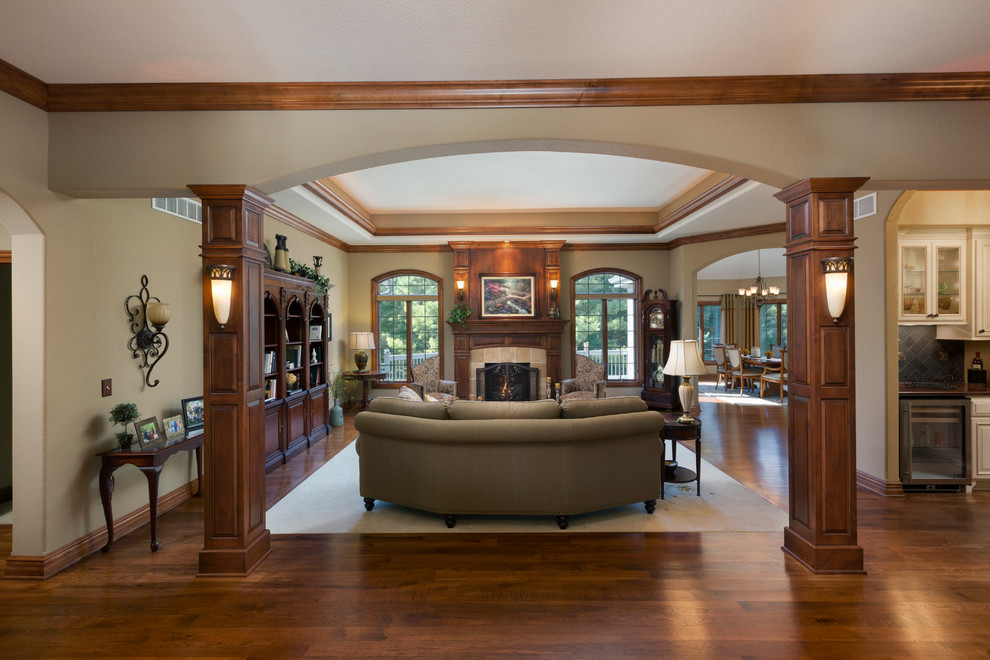 Пример оригинального дизайна: большая парадная гостиная комната в классическом стиле с бежевыми стенами, темным паркетным полом, стандартным камином, фасадом камина из дерева и коричневым полом