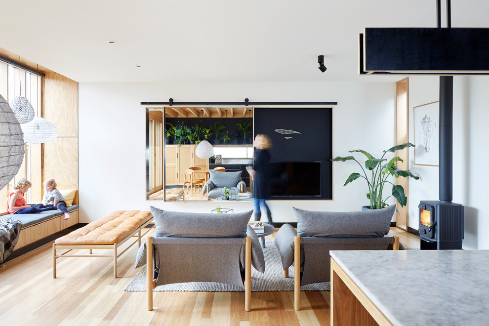 Idee per un piccolo soggiorno contemporaneo aperto con pareti bianche, parquet chiaro, stufa a legna e TV nascosta