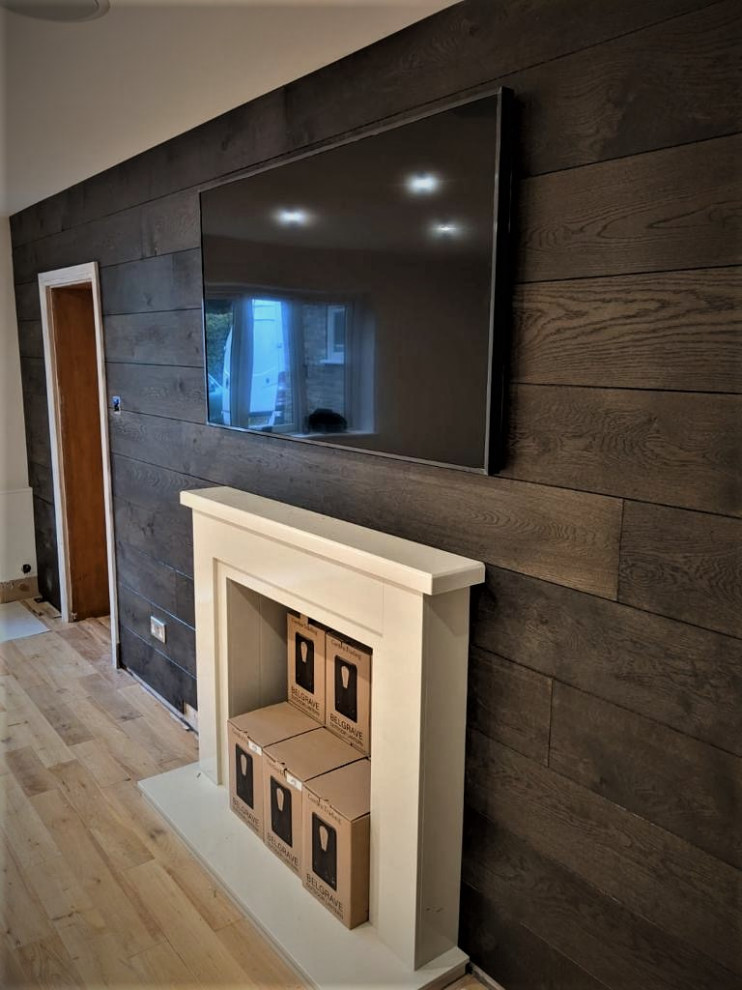 Ejemplo de salón abierto rústico grande con paredes marrones, suelo de madera clara, marco de chimenea de madera, televisor colgado en la pared, suelo marrón y madera