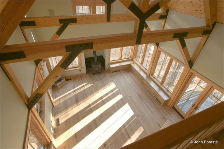 Modelo de salón abierto de estilo americano grande con paredes beige, suelo de madera clara, estufa de leña y marco de chimenea de metal