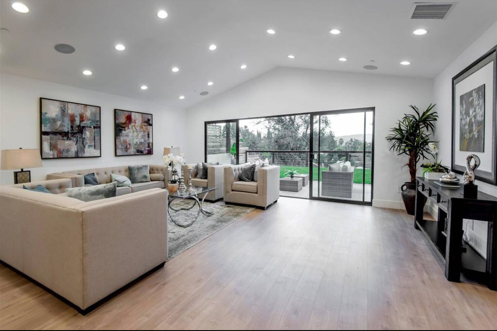 На фото: большая открытая гостиная комната в стиле модернизм с белыми стенами, светлым паркетным полом и коричневым полом без камина, телевизора