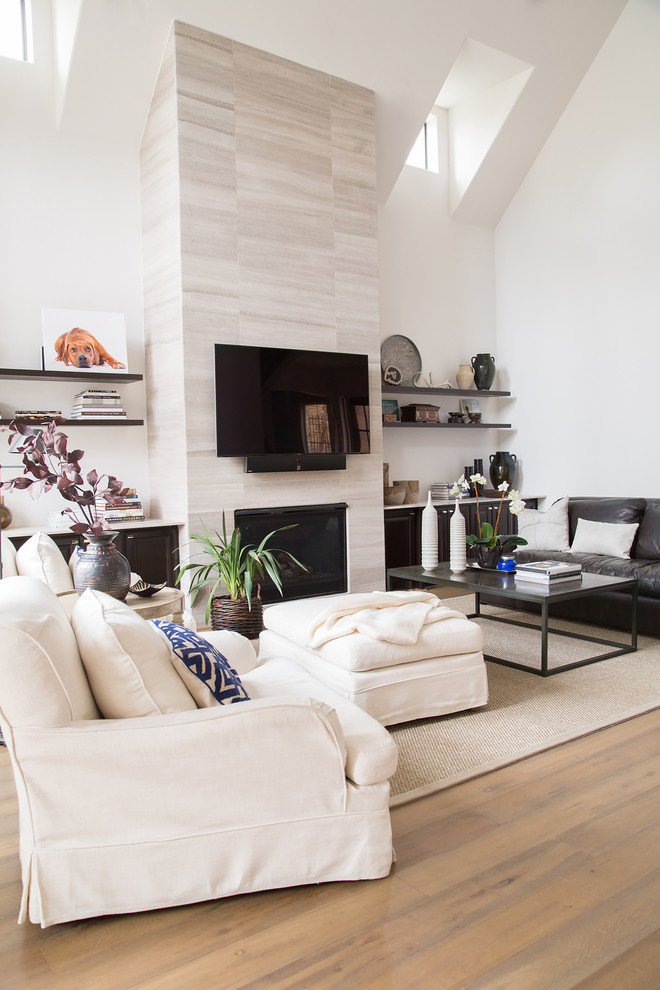 На фото: открытая гостиная комната в стиле неоклассика (современная классика) с белыми стенами, паркетным полом среднего тона, фасадом камина из камня, телевизором на стене, стандартным камином и ковром на полу