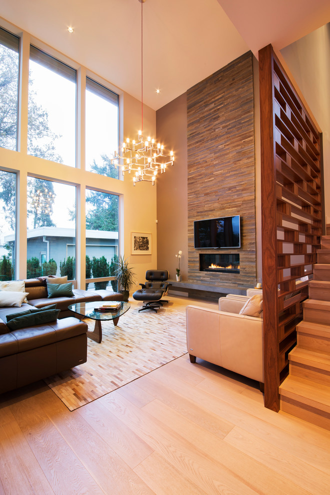 Modelo de salón abierto actual con paredes beige, suelo de madera clara, chimenea lineal, marco de chimenea de piedra y televisor colgado en la pared