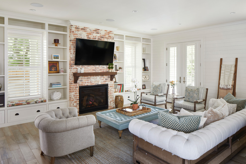 Idée de décoration pour un grand salon champêtre ouvert avec un mur blanc, une cheminée standard, un manteau de cheminée en brique, un téléviseur fixé au mur, un sol en bois brun et un sol marron.