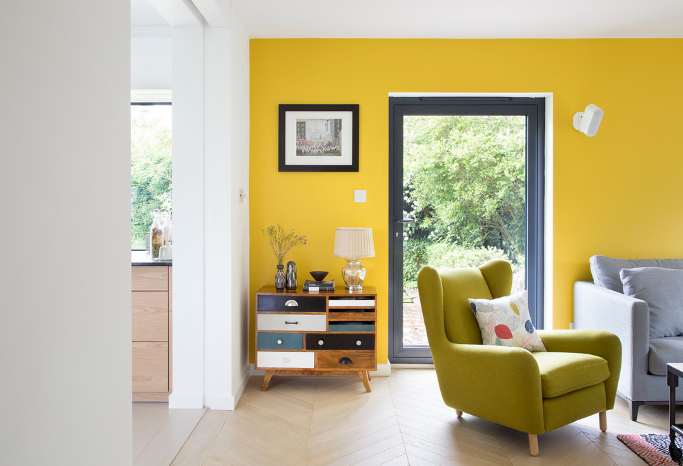 Photo of a medium sized bohemian grey and yellow open plan living room in London with a wall mounted tv, yellow walls, feature lighting, light hardwood flooring and beige floors.