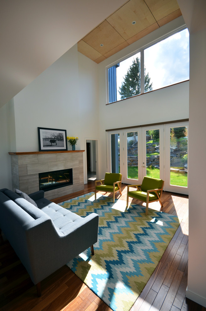 Offenes Modernes Wohnzimmer mit weißer Wandfarbe, braunem Holzboden, Kamin und Kaminumrandung aus Stein in Calgary