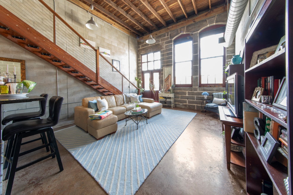 Urban mezzanine living room in Tampa with concrete flooring, a freestanding tv, brown floors, exposed beams and brick walls.