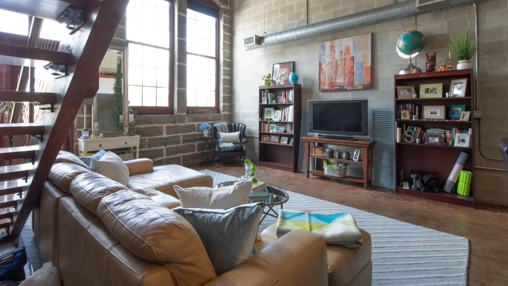 Example of an urban loft-style concrete floor, brown floor, exposed beam and brick wall living room library design in Tampa with gray walls, no fireplace and a tv stand