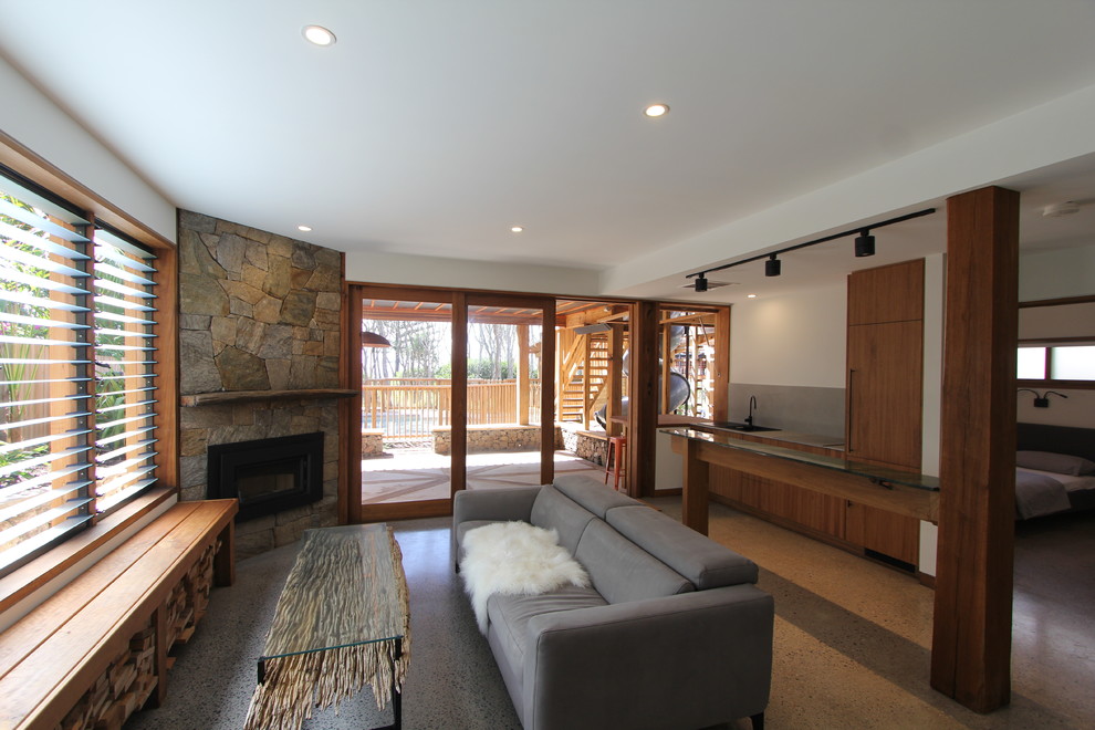 サンシャインコーストにある小さなラスティックスタイルのおしゃれなLDK (コンクリートの床、コーナー設置型暖炉、石材の暖炉まわり、グレーの床) の写真