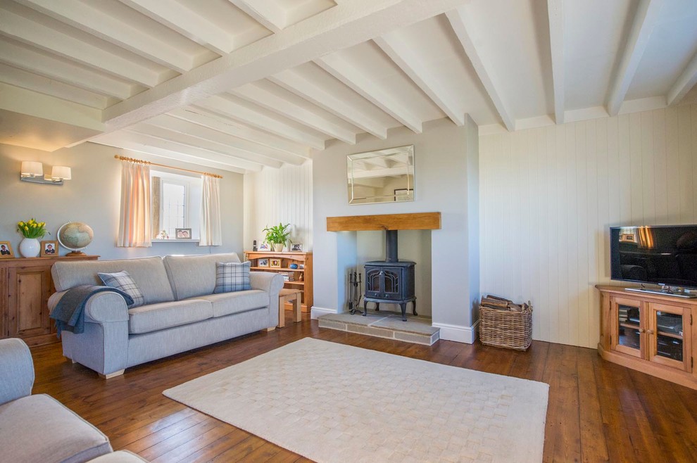 Immagine di un soggiorno country con pareti bianche, pavimento in legno massello medio, stufa a legna, cornice del camino in legno e TV autoportante