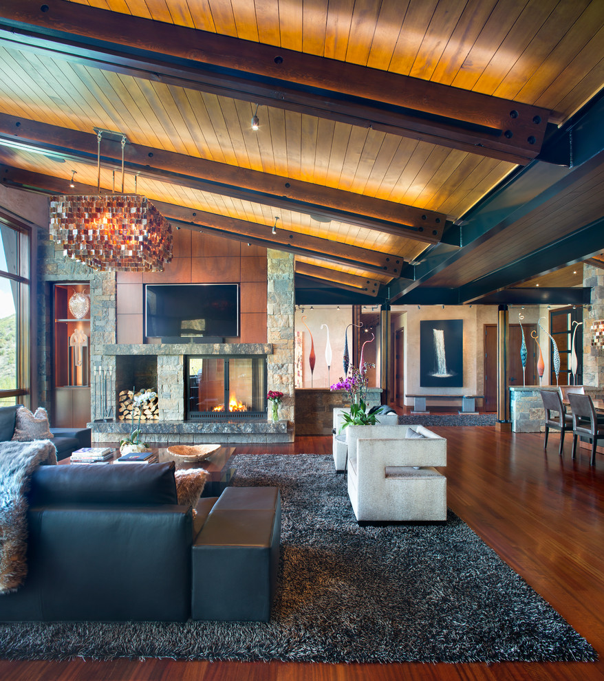 Offenes Uriges Wohnzimmer mit brauner Wandfarbe, braunem Holzboden, Tunnelkamin, Kaminumrandung aus Stein, TV-Wand und braunem Boden in Denver