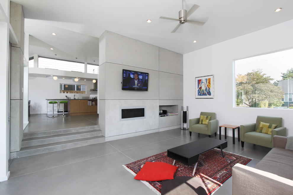 Bild på ett mellanstort funkis separat vardagsrum, med betonggolv, ett finrum, vita väggar, en bred öppen spis, en spiselkrans i betong, en väggmonterad TV och grått golv