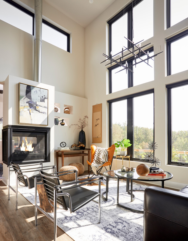 This is an example of a small contemporary open plan living room in DC Metro with white walls, medium hardwood flooring, a two-sided fireplace, a plastered fireplace surround, no tv and brown floors.