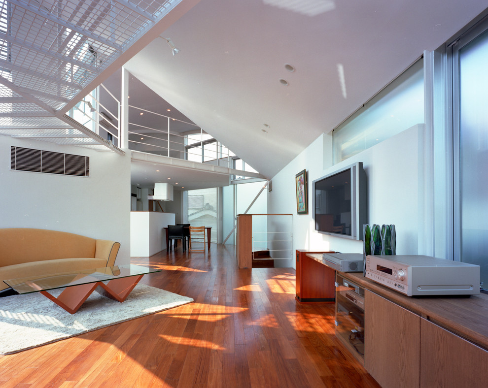 Modelo de salón abierto contemporáneo de tamaño medio sin chimenea con paredes blancas, televisor colgado en la pared, suelo marrón y suelo de madera en tonos medios