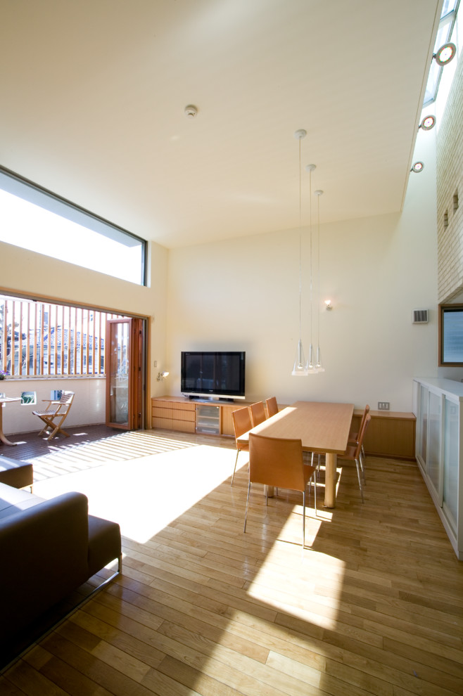 Offenes Modernes Wohnzimmer mit weißer Wandfarbe, braunem Holzboden, freistehendem TV und braunem Boden in Sonstige
