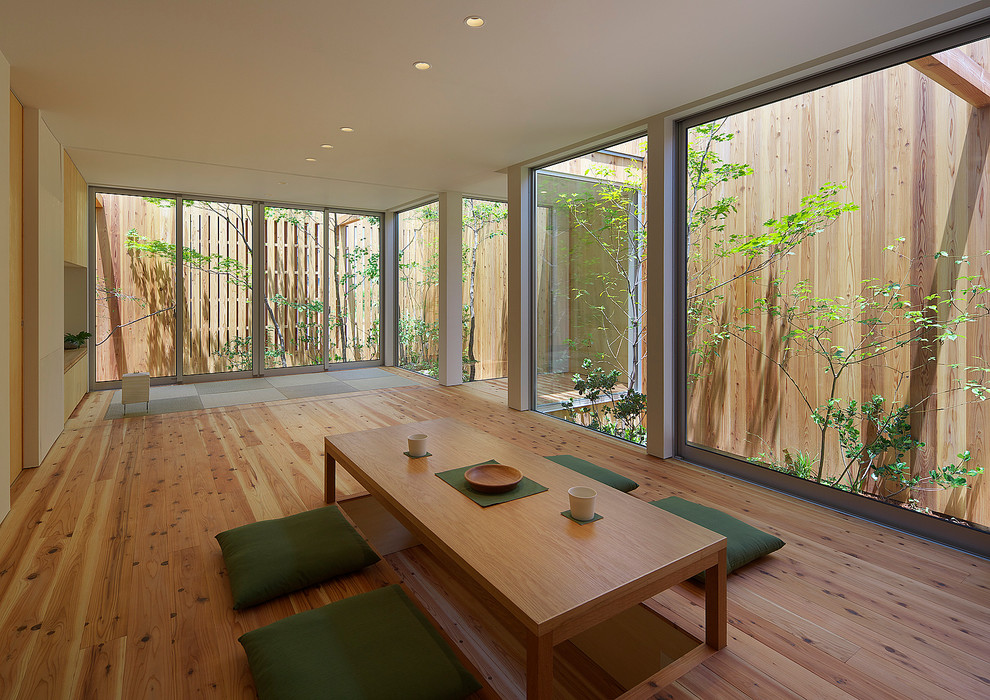 Modelo de salón abierto de estilo zen de tamaño medio con paredes blancas, suelo de madera clara, suelo marrón y televisor independiente