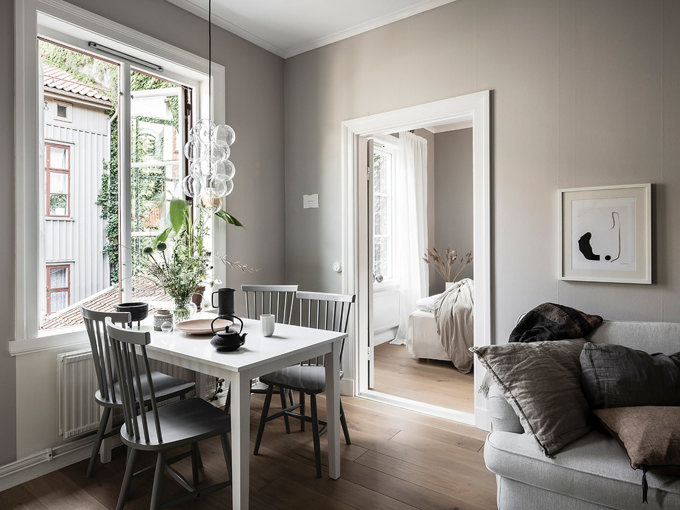 Cette image montre une petite salle à manger ouverte sur le salon nordique avec un mur gris, un sol en bois brun et un sol beige.