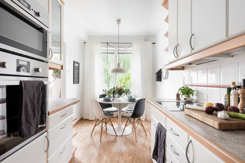 Modelo de comedor de cocina escandinavo pequeño con suelo de madera en tonos medios, paredes blancas y suelo marrón
