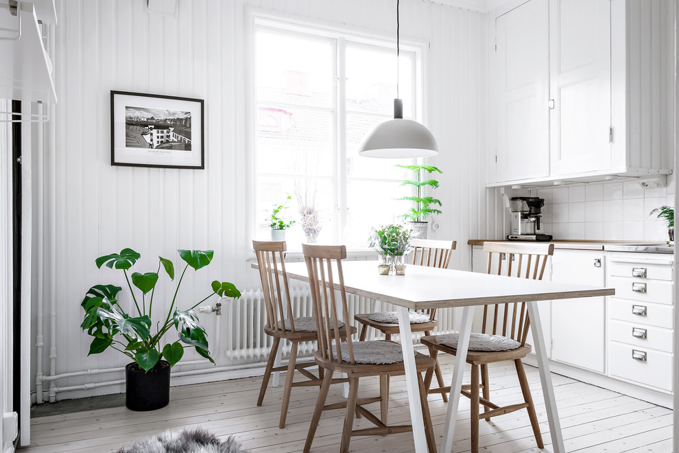 На фото: кухня-столовая в скандинавском стиле с светлым паркетным полом, белым полом и белыми стенами