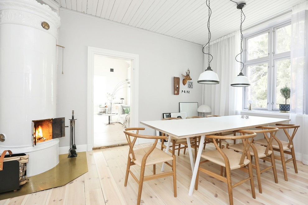 Diseño de comedor nórdico de tamaño medio con paredes blancas, suelo de madera clara, estufa de leña y suelo beige