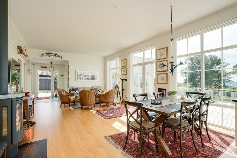 Photo of a medium sized coastal dining room in Gothenburg with white walls, light hardwood flooring, a wood burning stove and a tiled fireplace surround.