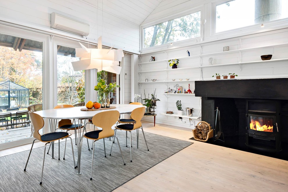 Bild på en skandinavisk matplats med öppen planlösning, med vita väggar, ljust trägolv, en öppen vedspis och beiget golv