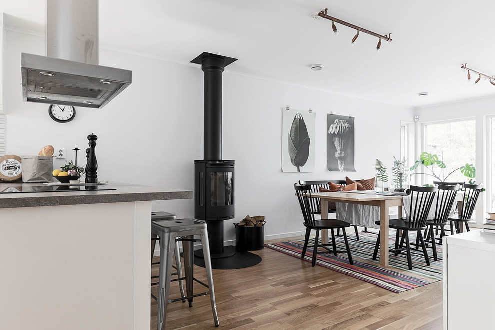 ストックホルムにある北欧スタイルのおしゃれなダイニングキッチン (白い壁、無垢フローリング、薪ストーブ、金属の暖炉まわり、茶色い床) の写真