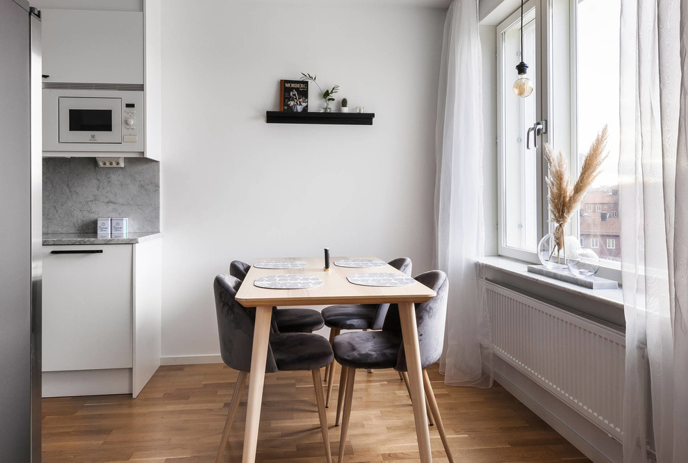 Skandinavisk inredning av ett kök med matplats, med vita väggar, mellanmörkt trägolv och brunt golv