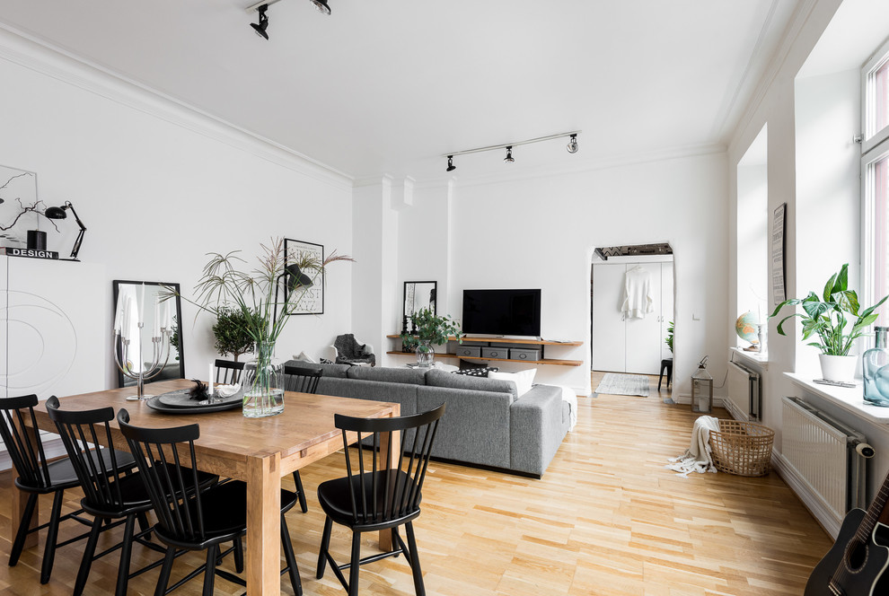Aménagement d'une salle à manger ouverte sur le salon scandinave avec un mur blanc et parquet clair.