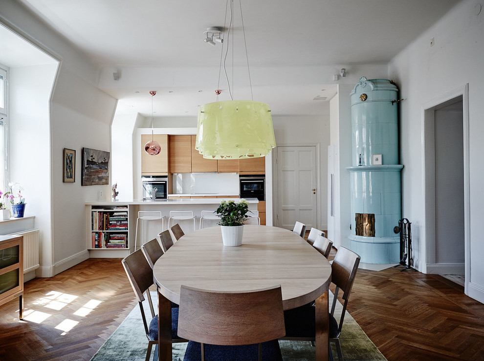 На фото: кухня-столовая в скандинавском стиле с белыми стенами, темным паркетным полом и угловым камином с